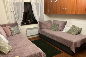 Een slaapkamer met twee bedden, een radiator, een raam met gordijnen en een houten garderobe.