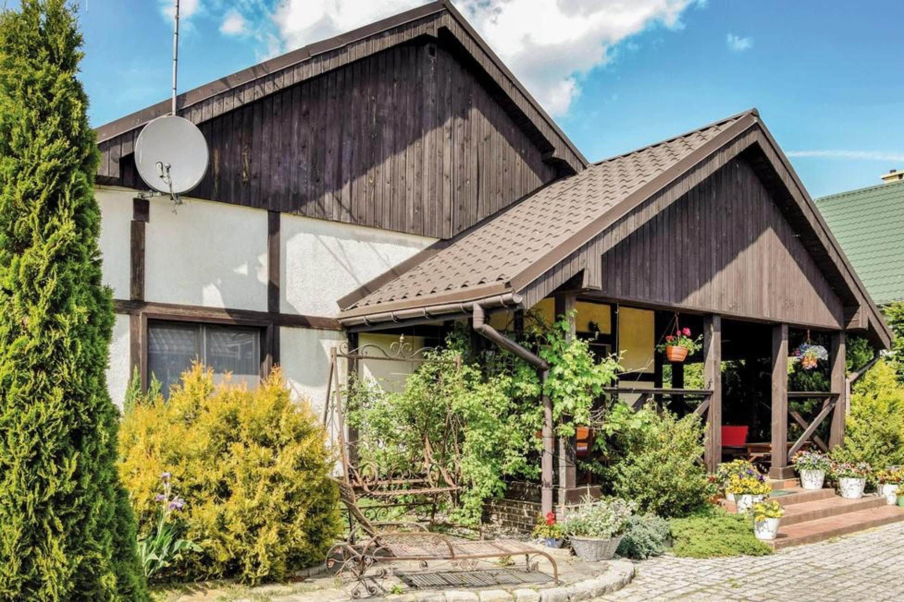 Ein traditionelles Holzhaus mit geneigtem Dach, einer Satellitenschüssel und einem Garten mit Blumentöpfen.