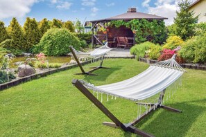 Een tuin met twee hangmatten, een houten terras en een prieel.