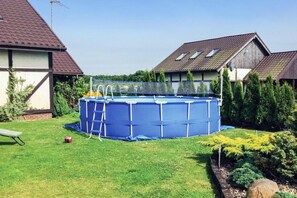 Un jardin avec une piscine hors sol bleue, une échelle et un petit trampoline.