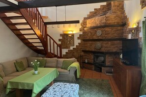 Un salon chaleureux avec un escalier en bois, une cheminée, un canapé et une table.