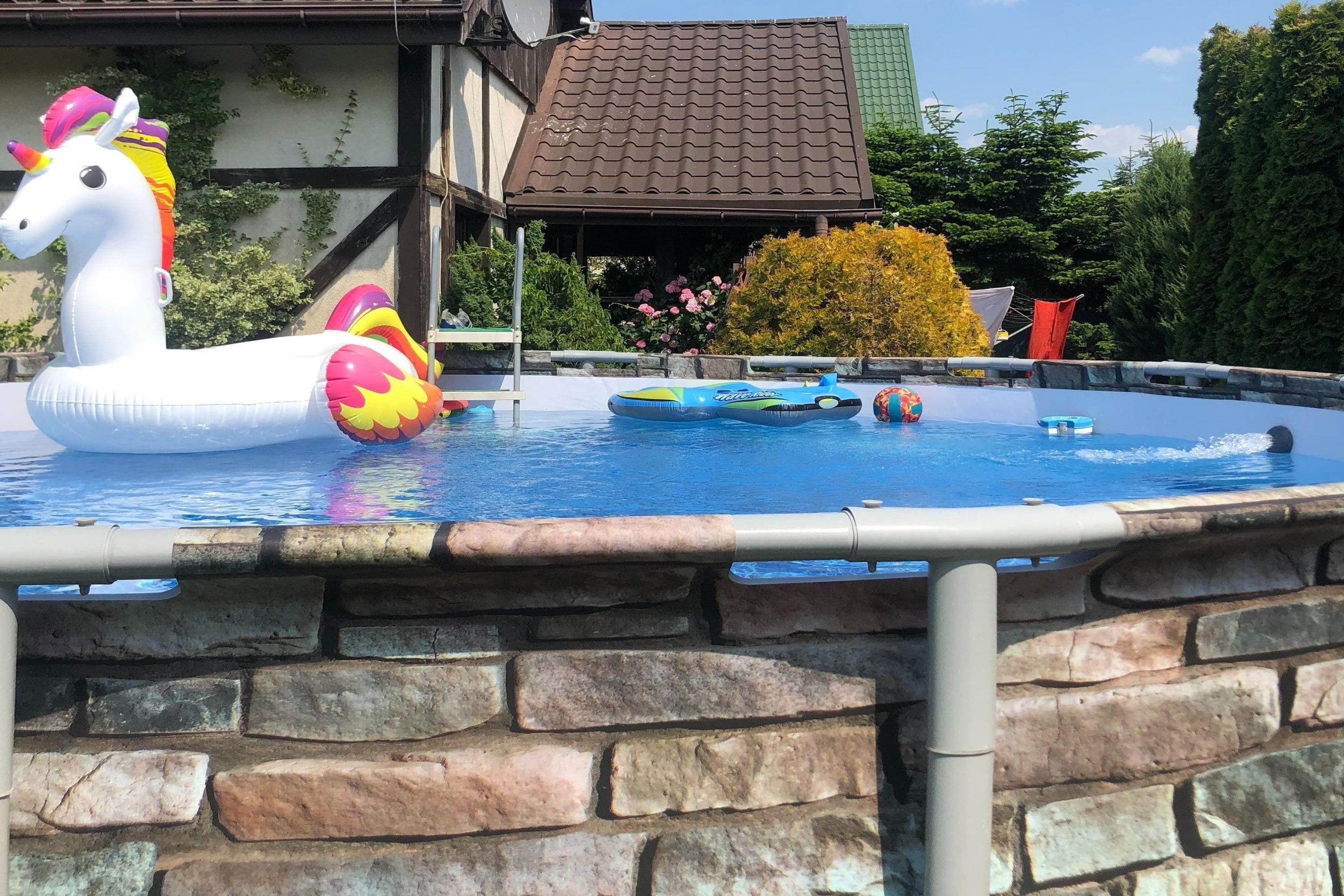 A swimming pool with a unicorn float, a small boat, and a stone wall.