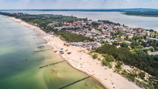 An aerial view of a coastal town with a sandy beach, a marina, and residential buildings. - Comfortable Holiday Home With Garden, by the Lake (gmina Będzino)