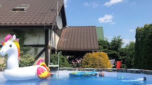 A swimming pool with inflatable toys, a stone wall, and a building with a tiled roof. - Comfortable Holiday Home With Garden, by the Lake (gmina Będzino)