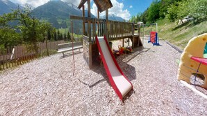 A playground with a slide and climbing structures, surrounded by a wooden fence and set against a mountainous backdrop. - Chalet in Wildkogel Near Ski Slopes (Neukirchen am Grossvenediger)