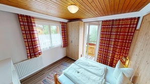 A bedroom with a wooden bed, plaid curtains, and a view of a wooden deck outside. - Chalet in Wildkogel Near Ski Slopes (Neukirchen am Grossvenediger)
