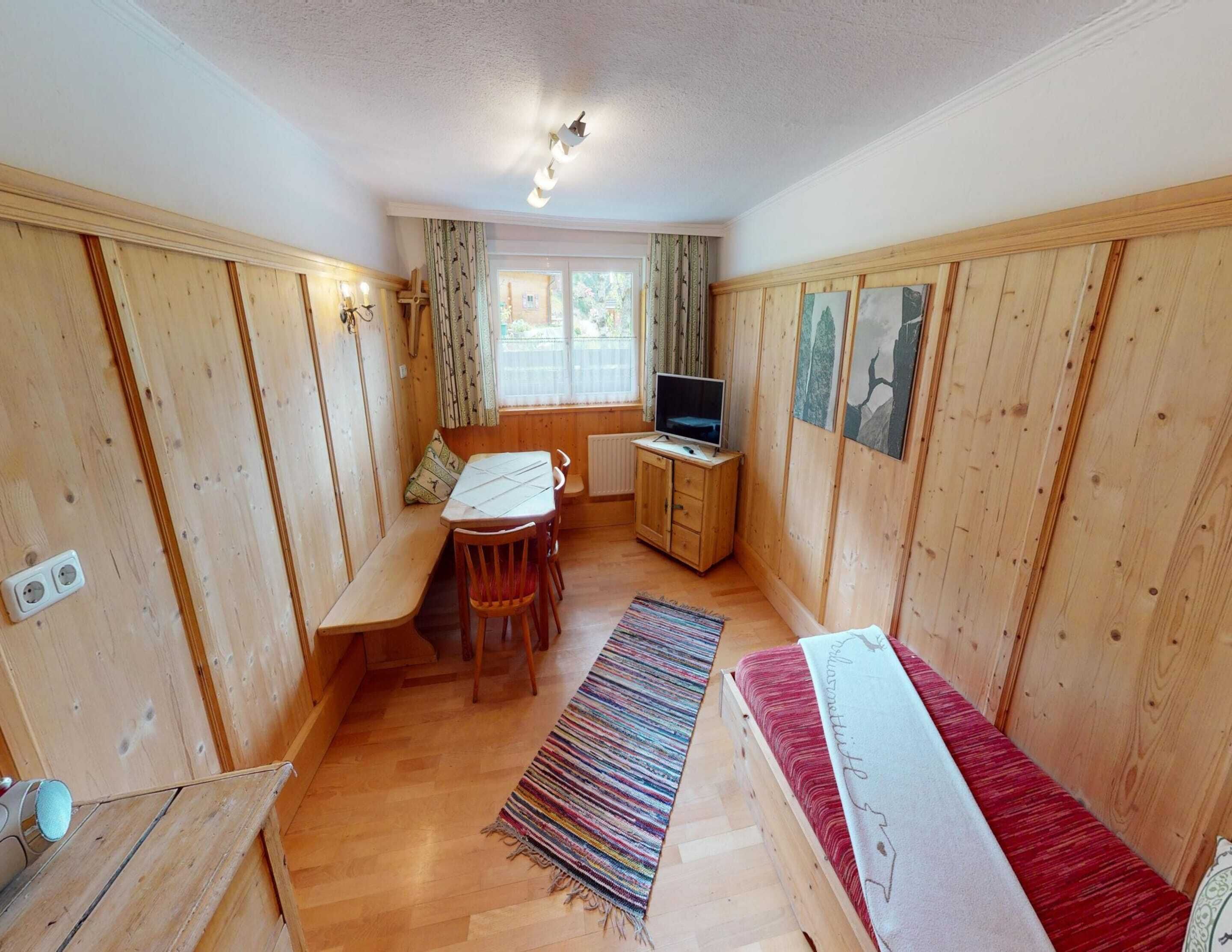 A compact room with wooden paneling, a dining table with chairs, a TV on a cabinet, and a bench.