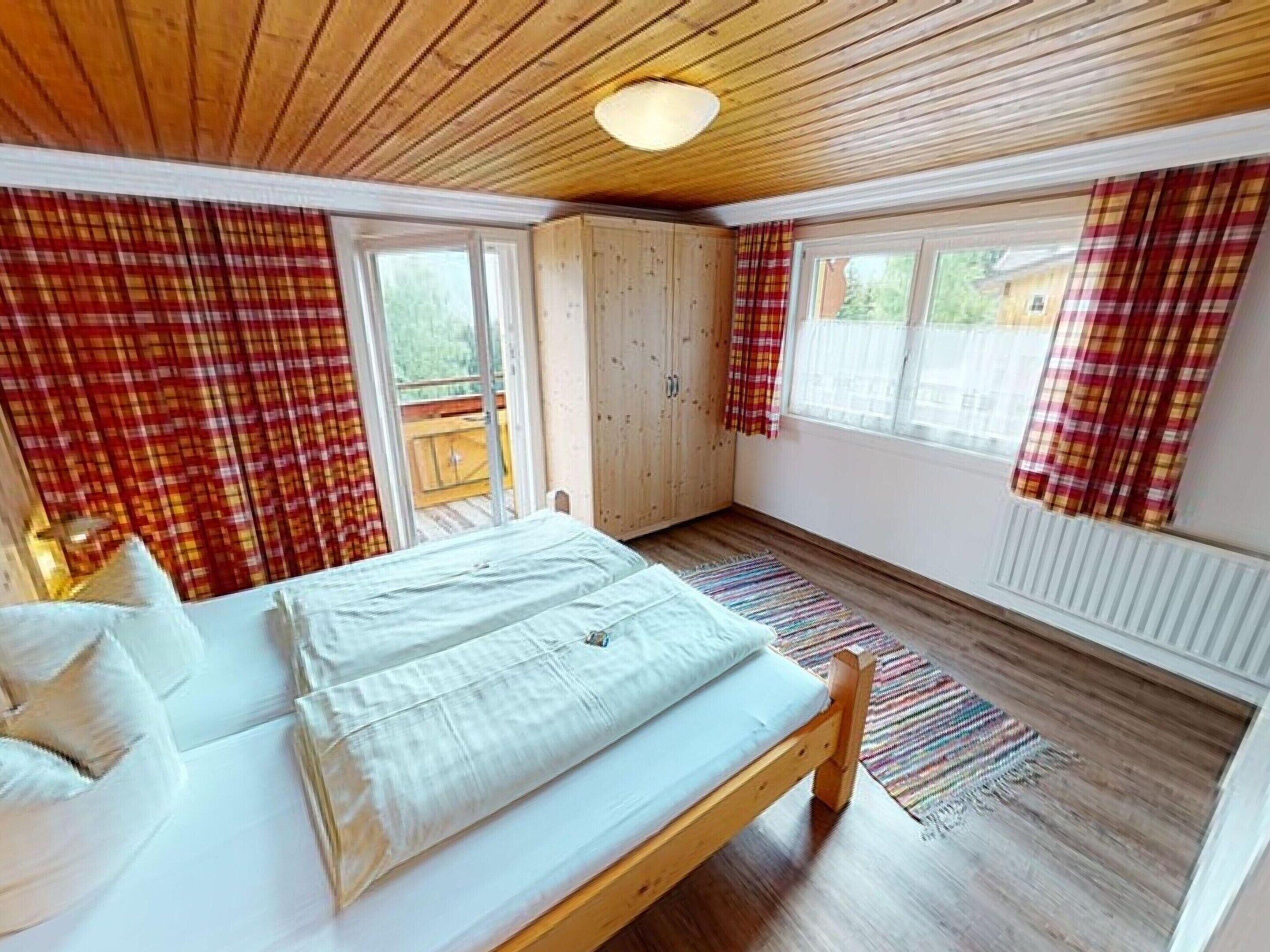 Une chambre à coucher avec un lit en bois, une armoire et une fenêtre ornée de rideaux à carreaux.
