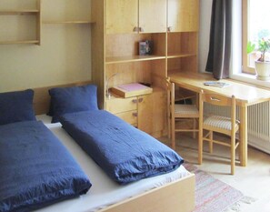 Ein Schlafzimmer mit zwei Betten, einem Holztisch, einem Stuhl und einem Fenster mit Vorhängen.