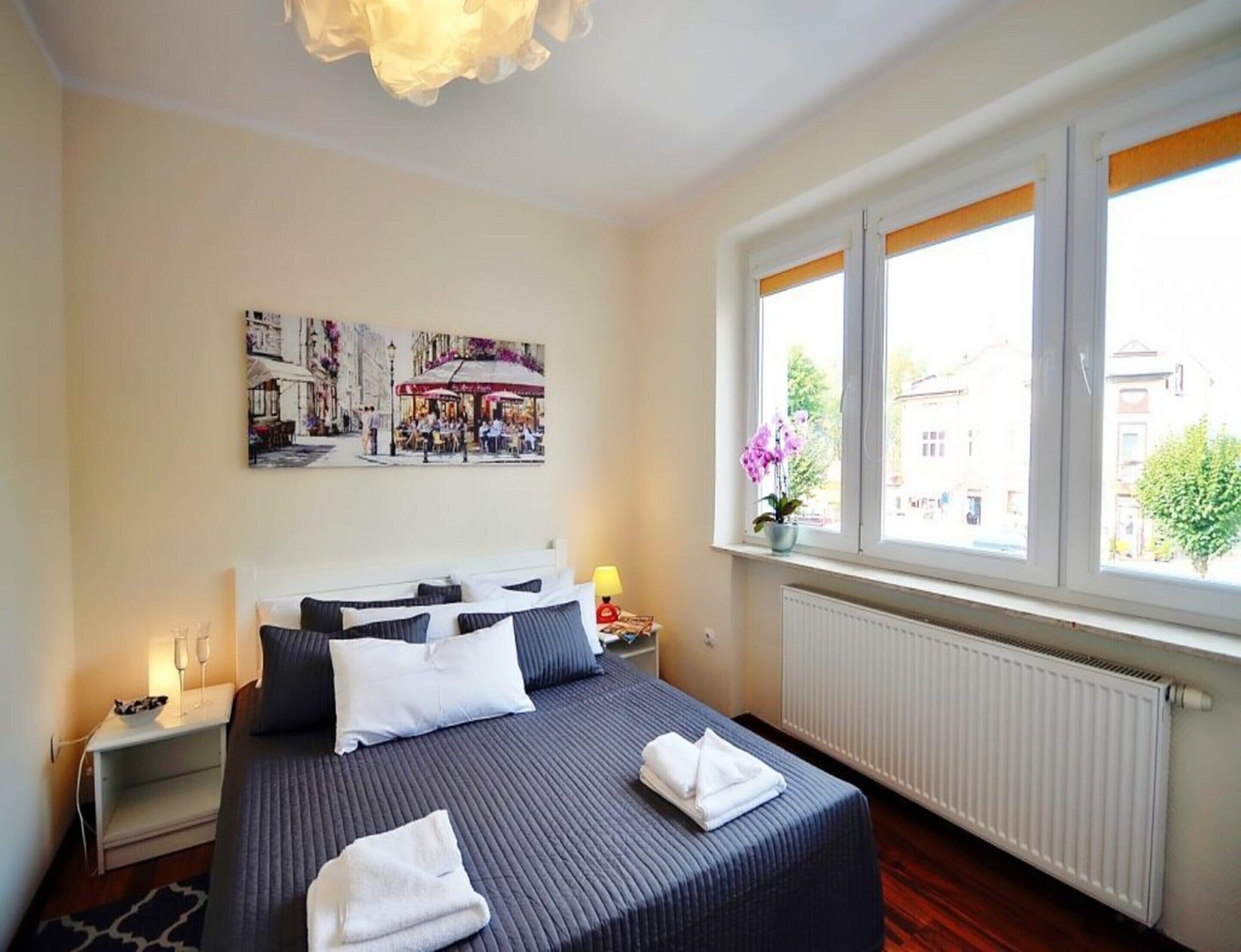 Ein Hotelzimmer mit einem großen Bett, einem Nachttisch mit Lampe, einem Fenster mit Blick auf die Stadt und einem Gemälde an der Wand.