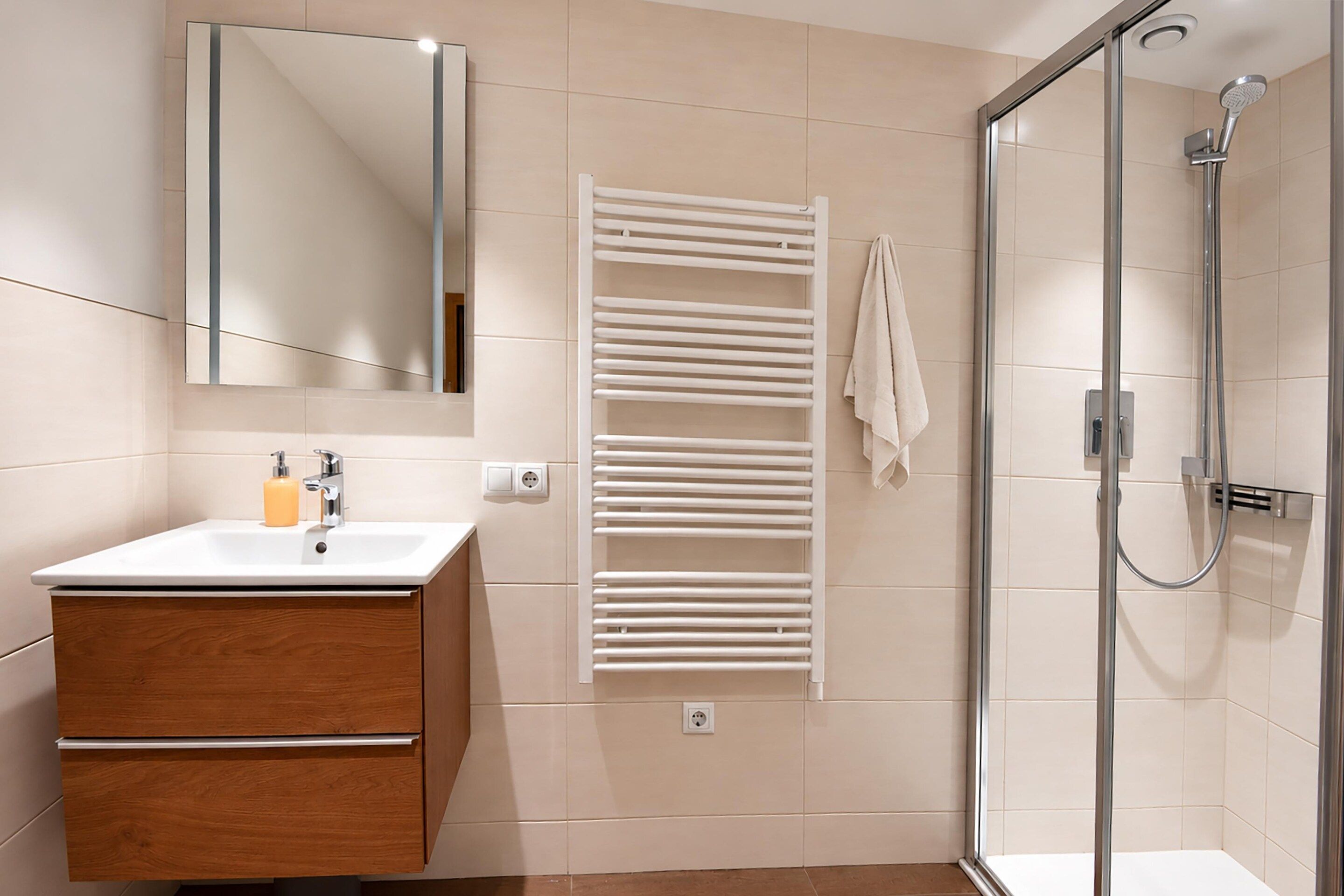 A modern bathroom with a glass shower enclosure, a white towel rack, and a wooden vanity with a mirror.