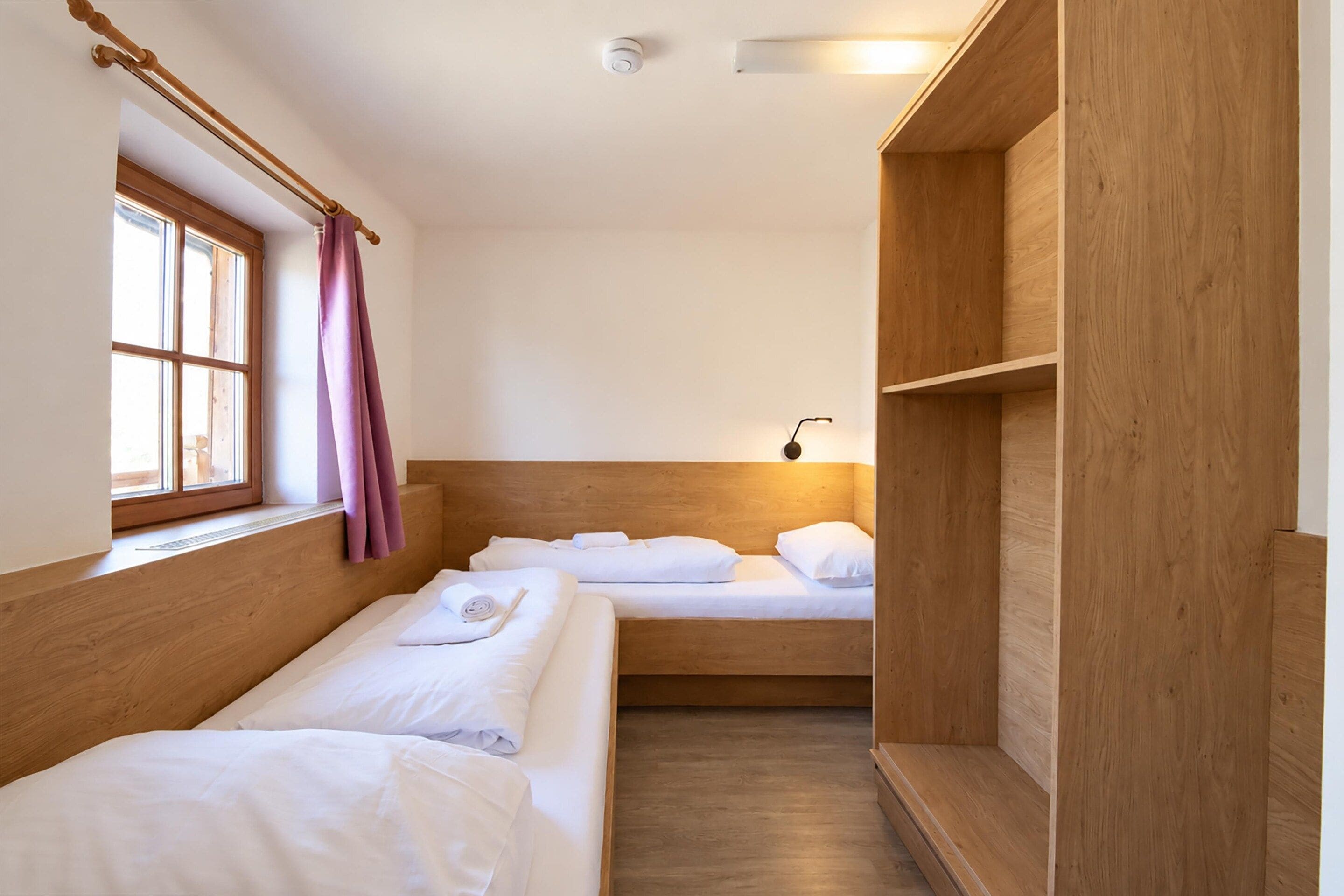 Een kamer met twee bedden, een raam met gordijnen, een nachtkastje en een wandlamp.
