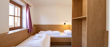 A room with two beds, a window with curtains, a bedside table, and a wall-mounted light.