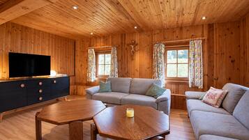 A wooden interior with a sofa, two tables, a TV, and curtains.