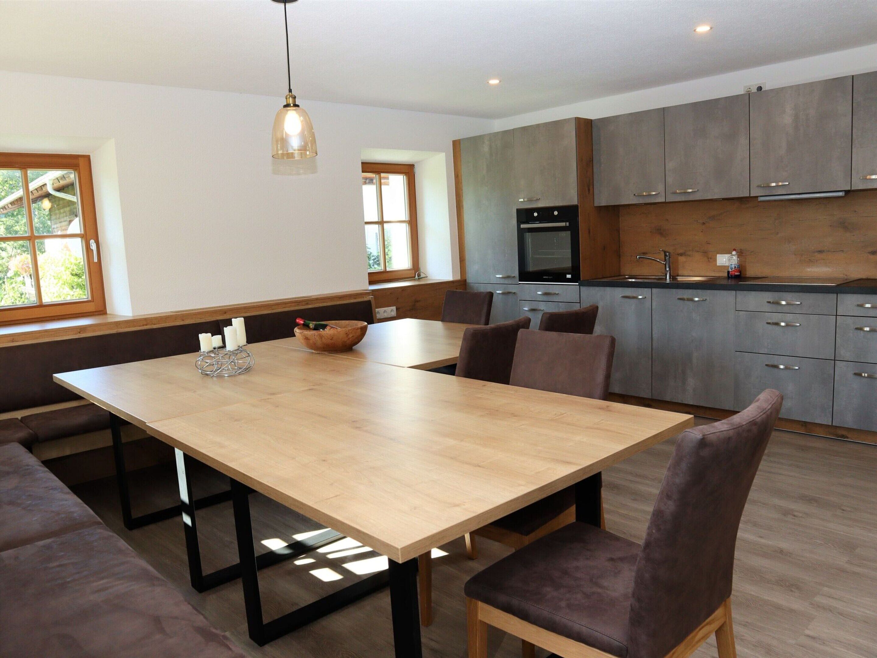 A modern kitchen with grey cabinets, a wooden dining table, and a built-in oven.