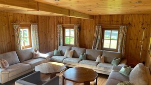 Un salon chaleureux avec des murs et des planchers en bois, un canapé d’angle, une petite table et un fauteuil.