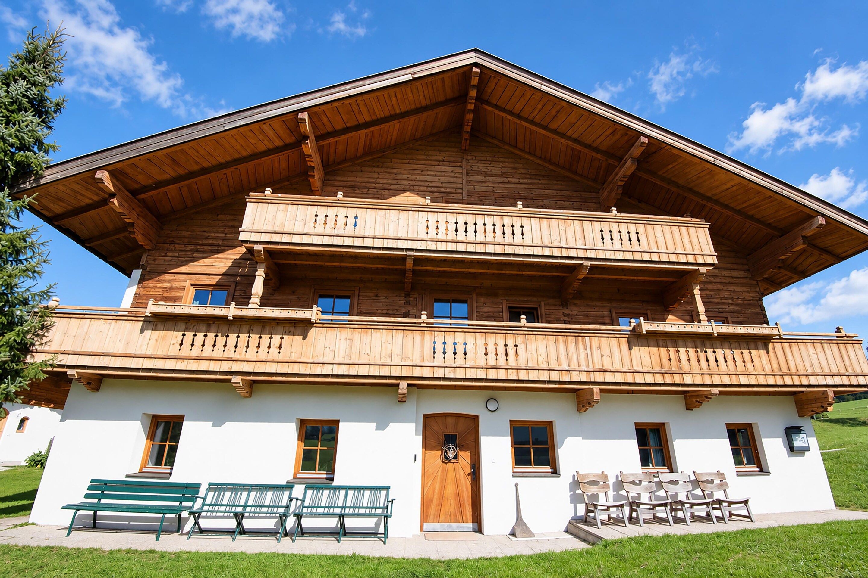 Un chalet de madera de dos pisos con balcones, una puerta principal y un banco afuera.