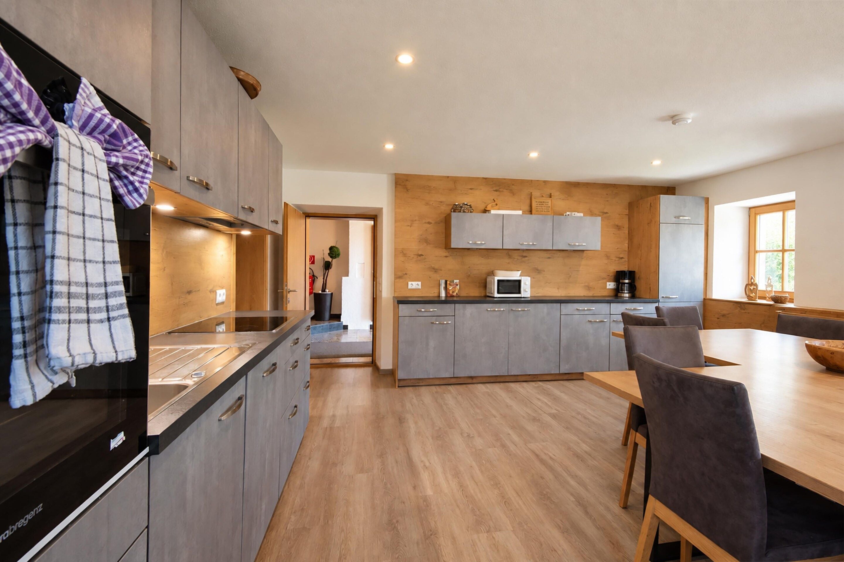 Una cocina moderna con gabinetes grises, un lavamanos de acero inoxidable y una mesa de comedor de madera con sillas.
