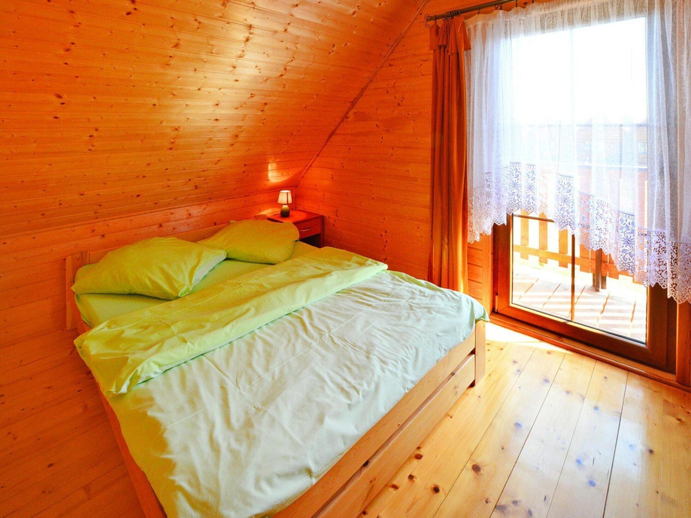 A wooden cabin bedroom with a bed, a nightstand, and a window with a view of a wooden deck.