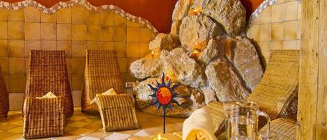 A spa room with a stone wall, two wicker chairs, a wooden bench, and a sun-shaped decoration.