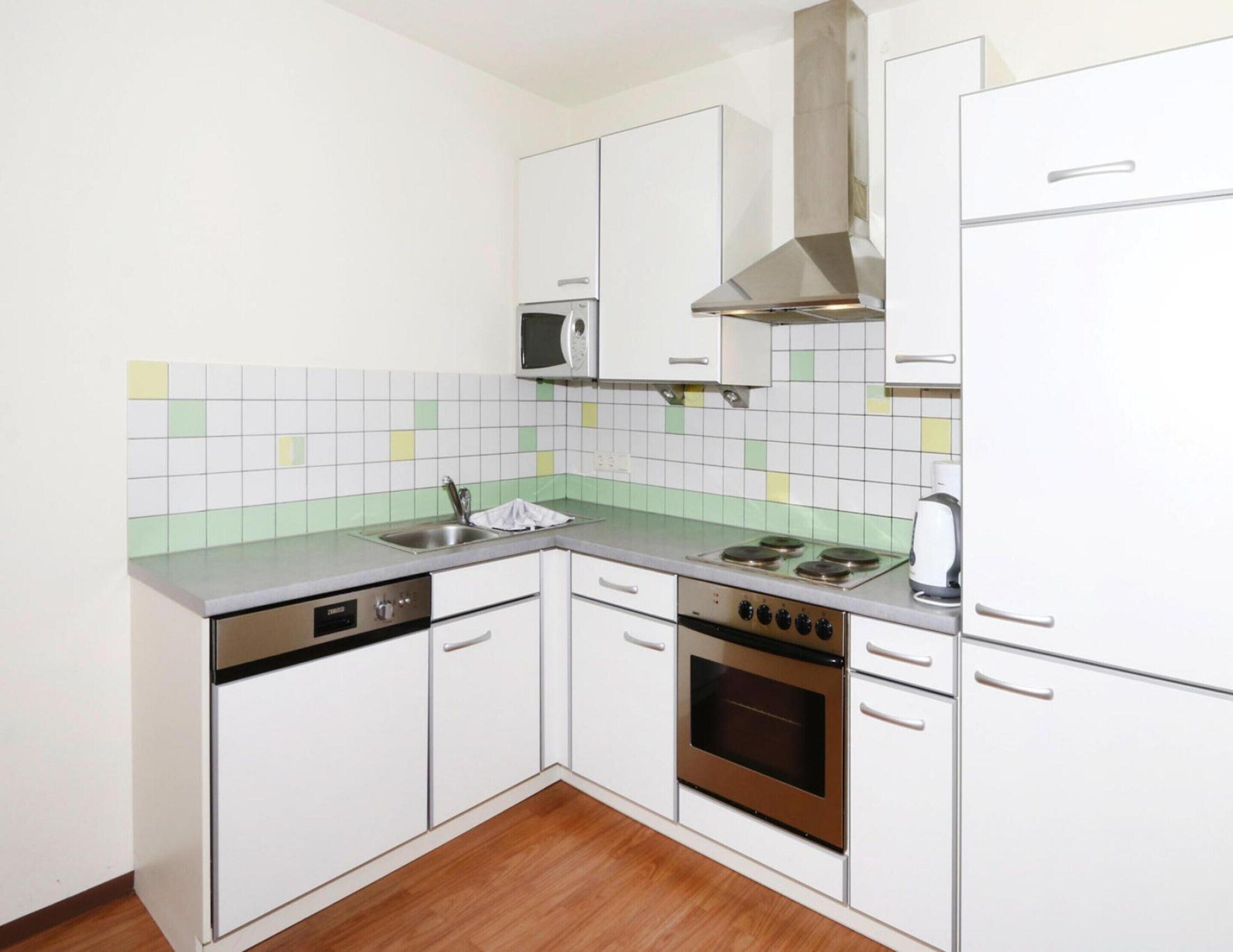 A compact kitchen with white cabinets, a stainless steel stove, a microwave, and a sink.