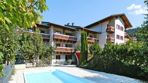 Ein Hotel mit Pool, mehreren Balkonen und einer Bergkulisse.