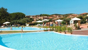 A large outdoor swimming pool surrounded by lounge chairs and umbrellas, with buildings in the background. - Apartment in Holiday Complex Only 100 m From the Beach (Golfo Aranci)