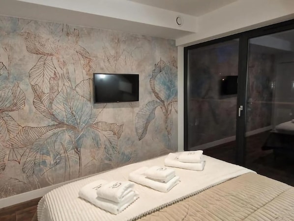 Quarto de hotel com uma cama grande, televisão de tela plana na parede e porta de vidro que dá para uma varanda.