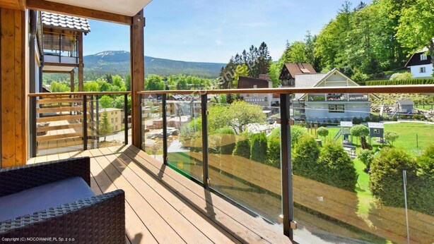 A wooden deck with a glass balustrade overlooking a residential area with houses and greenery. - Apartment, Beautiful View, Szklarska Poreba (Szklarska Poreba)