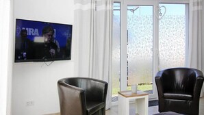 A living room with a flat-screen TV mounted on the wall, two leather armchairs, a small wooden table, and a sliding glass door leading to an outdoor area. - Ferienhaus, Boiensdorf (Boiensdorf)