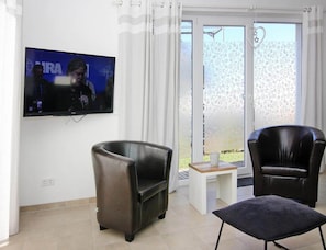 A living room with a flat-screen TV mounted on the wall, two leather armchairs, a small wooden table, and a sliding glass door leading to an outdoor area. - Ferienhaus, Boiensdorf (Boiensdorf)