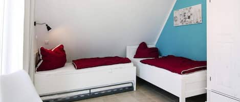 A room with two single beds, a white chair, and a white wardrobe.