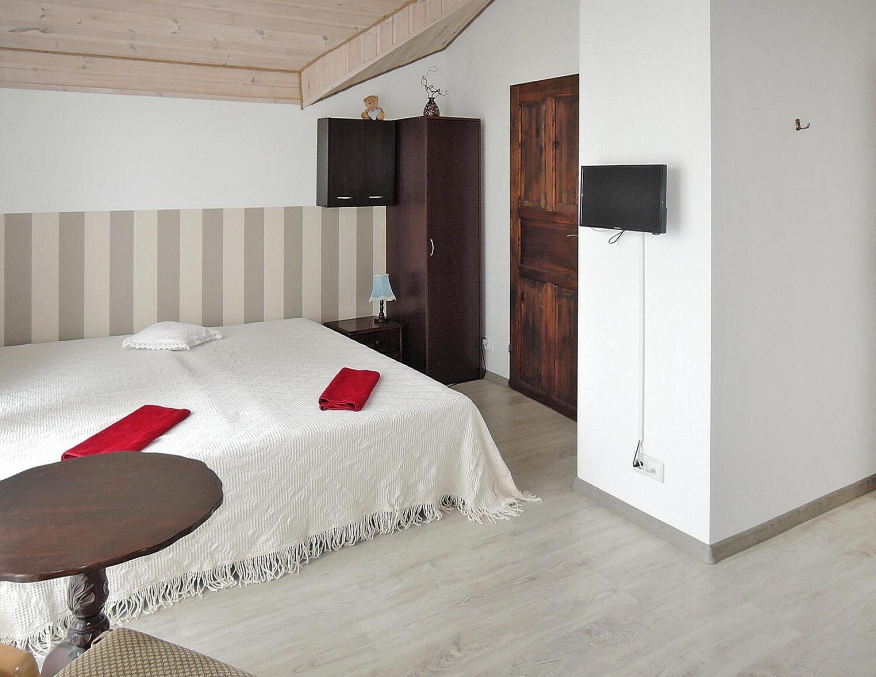 A bedroom with a bed, a bedside table, a wooden wardrobe, a TV mounted on the wall, and a door.