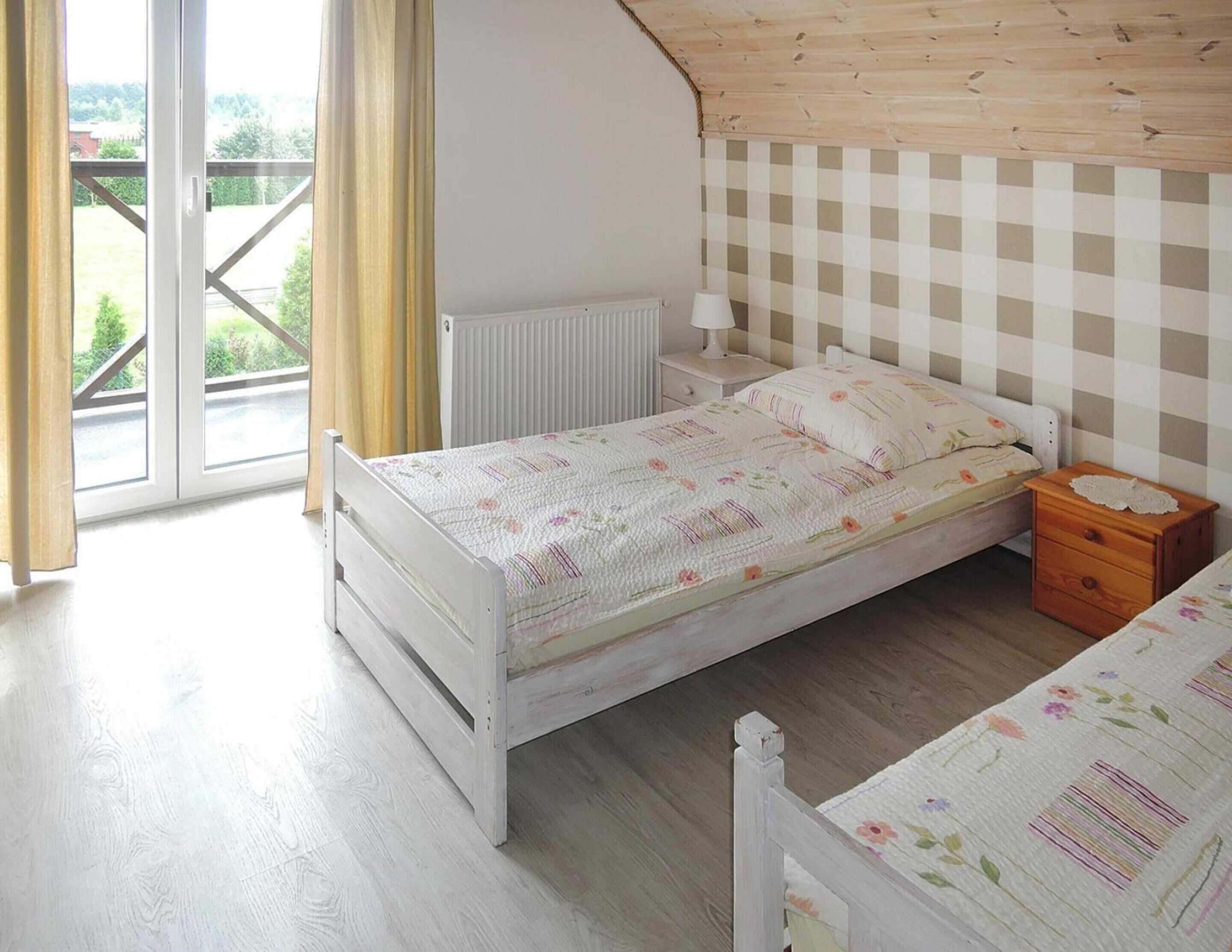 Een slaapkamer met een bed, nachtkastje, dressoir, radiator en een raam met gordijnen.