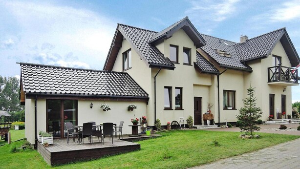 Ein zweistöckiges Haus mit Ziegeldach, einem Balkon und einer kleinen Veranda mit Gartenmöbeln.