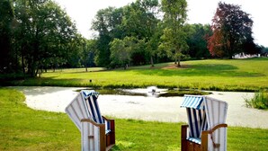 Twee rieten stoelen met streepkussens bij een vijver in een park.