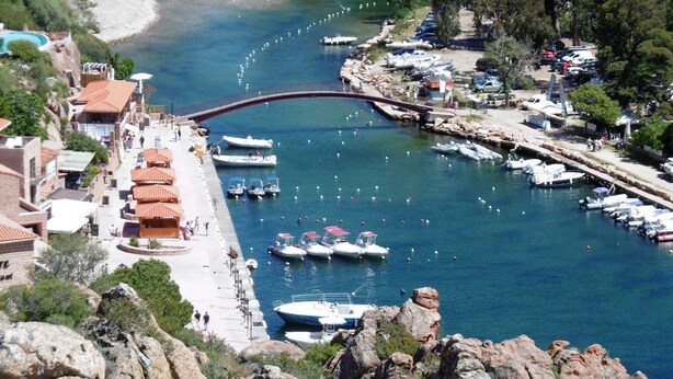 A coastal marina with boats docked, a bridge, and buildings along the waterfront.