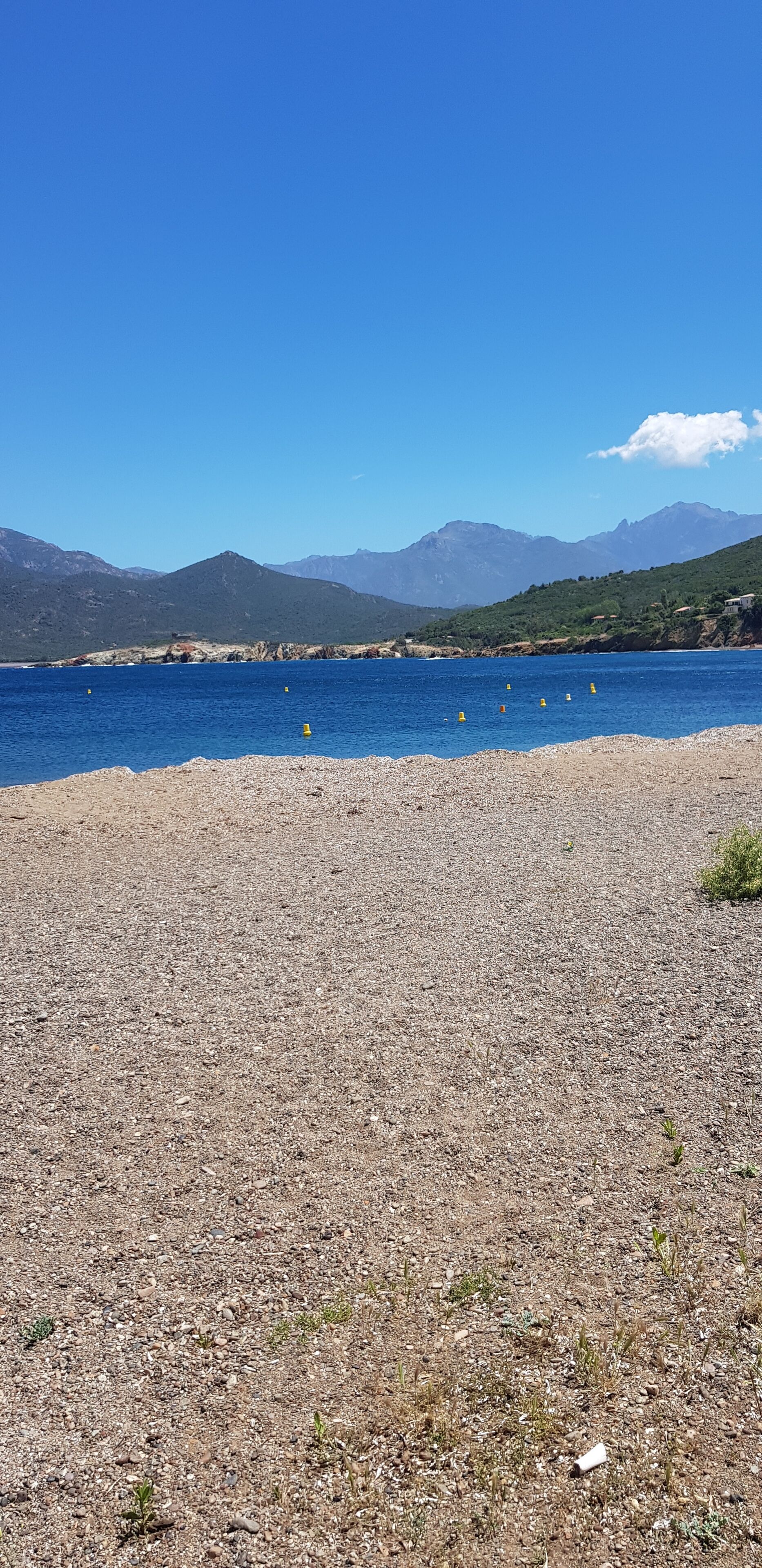 Une plage de galets bordée par une mer d’un bleu limpide et dominée par des montagnes lointaines.