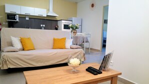 A living room with a sofa, a coffee table with a vase, and a kitchen area with appliances.