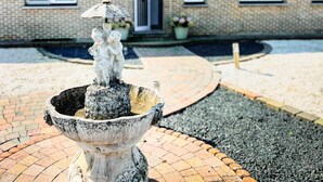 Ein Steinkonstrukt mit einer Kinderskulptur in einem Innenhof mit Backsteinwegen und einem Backsteingebäude im Hintergrund.