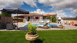 Un jardin avec une piscine, des chaises longues et une pergola ombragée par des parasols.