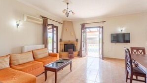Un salon comprenant un canapé, une table basse, une cheminée, un téléviseur et un coin repas avec des chaises.