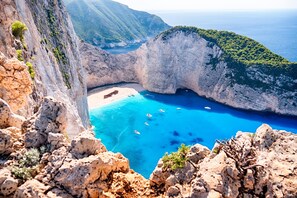 A coastal landscape with a rocky cliff, a beach, and clear blue waters.