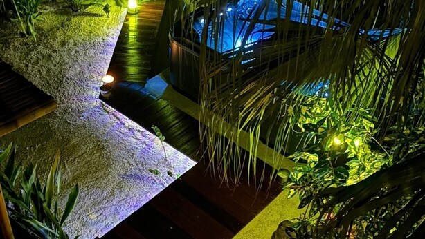 Un espacio al aire libre de temática tropical con una fuente de agua, asientos e iluminación ambiental.