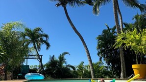 Una piscina con agua cristalina azul, rodeada de palmeras y una terraza de madera.