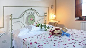 A neatly made bed with a floral bedspread, a decorative headboard, and a bedside lamp. - Agriturismo Poggio al Sole, Vinci (Vinci)
