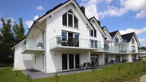 Ein modernes, zweistöckiges Haus mit Balkon, großen Fenstern und einer flachen Dachfläche.