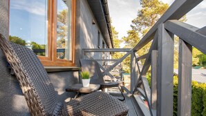 Terraza de madera con sillas de mimbre y una pequeña mesa, con vistas a una zona residencial.