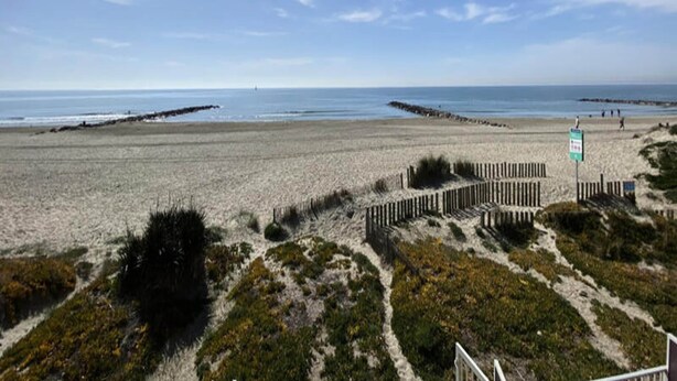 Una playa con una cerca de madera y un letrero, bajo un cielo despejado.