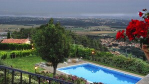 Una piscina circondata dal verde, vista su una città e un tramonto sullo sfondo.